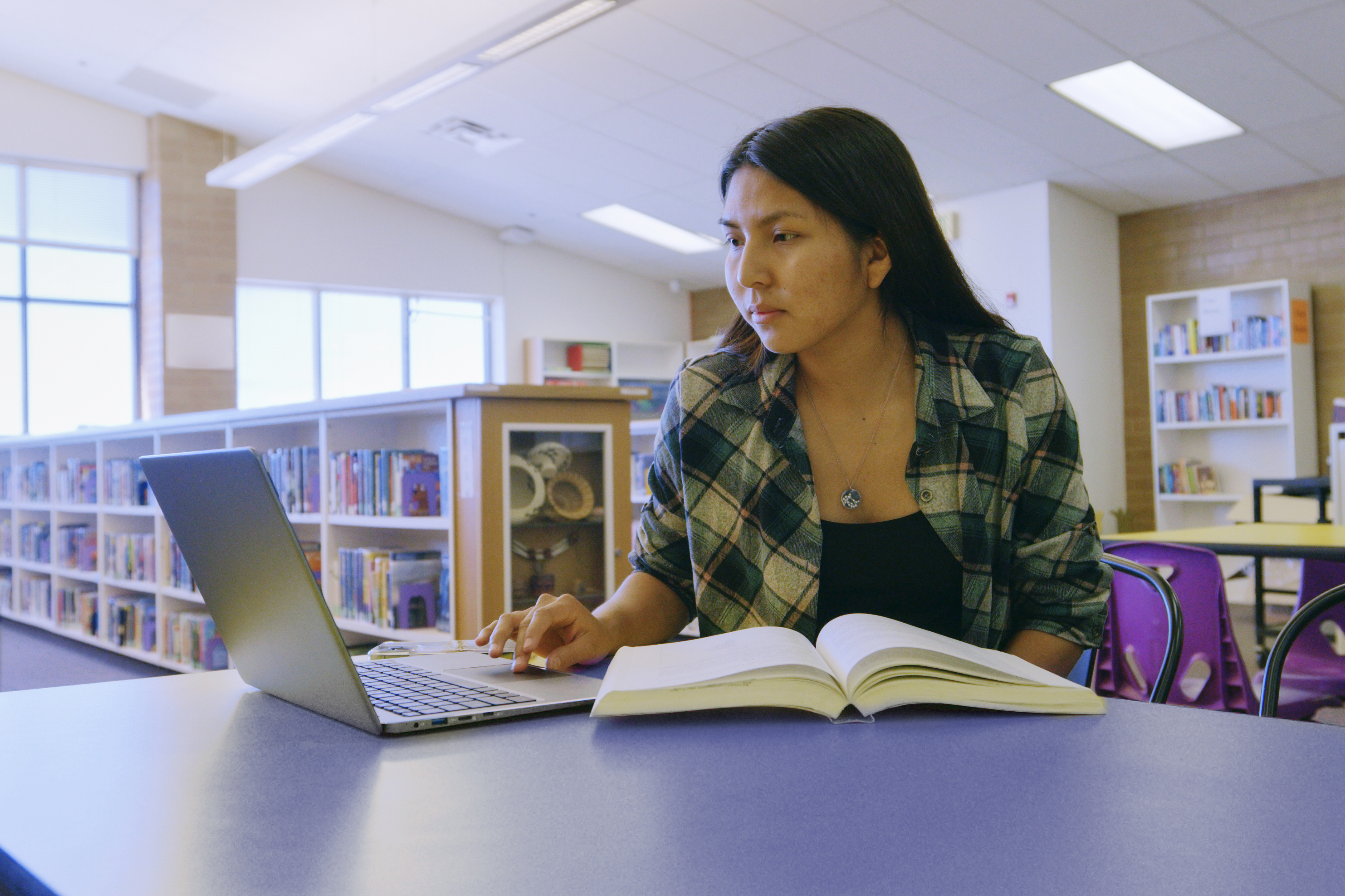 Young woman studying with a laptop and book at the library