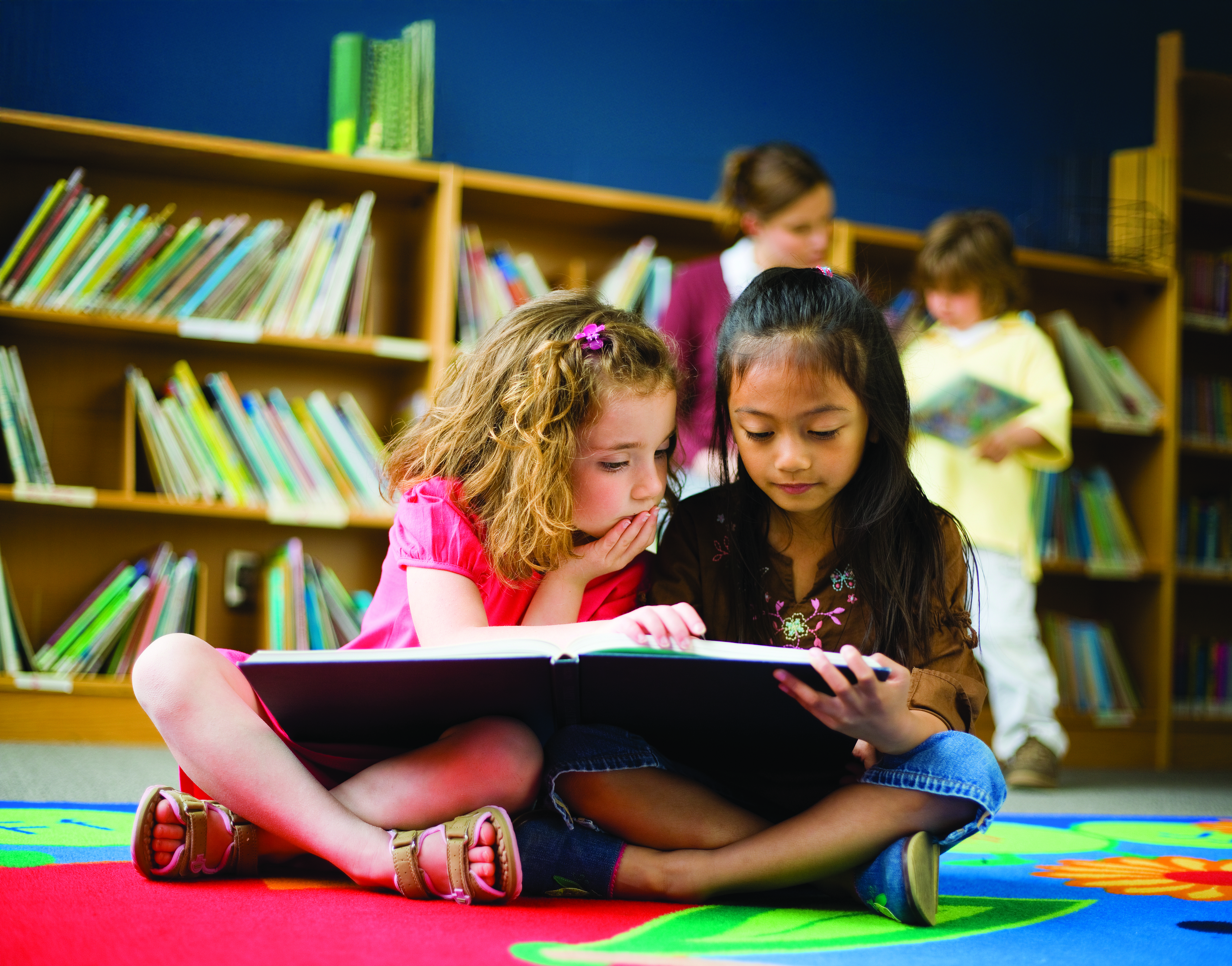 Two young girls reading a picture book together at the library